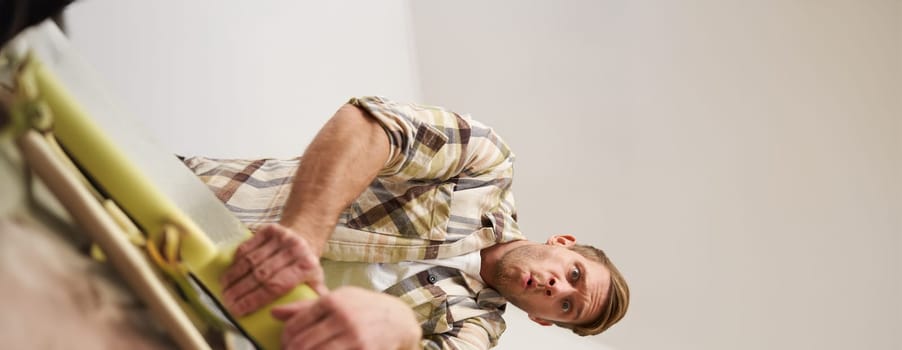 Vertical shot of man trying to press suitcase and close zipper, packing clothes for vacation. Tourist going on holiday, preparing for travelling abroad. Tourism concept