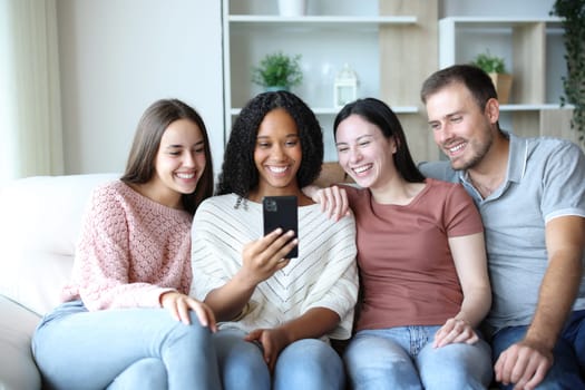 Four interracial friends at home checking mobile phone on a couch