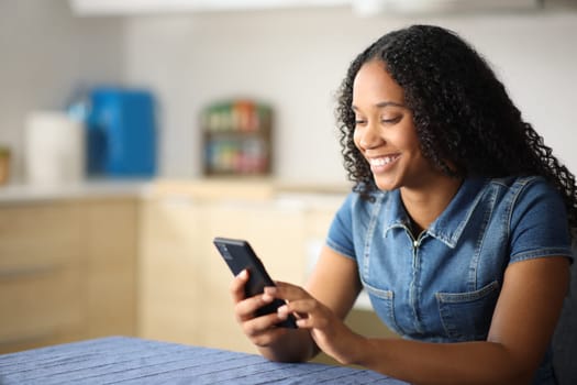 Happy black woman is using a mobile phone in a kitchen at home