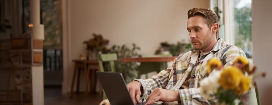 Lifestyle and workplace concept. Young handsome man in casual clothes, sitting in cafe with laptop, studying online, working remotely from coffee shop.