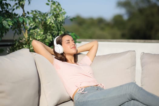 Happy woman relaxing listening audio with headphone outside sitting on a couch