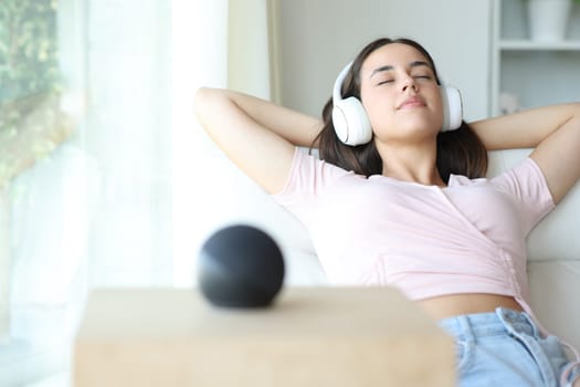 Woman relaxing listening music with headphone and smart speaker sitting on a sofa at home