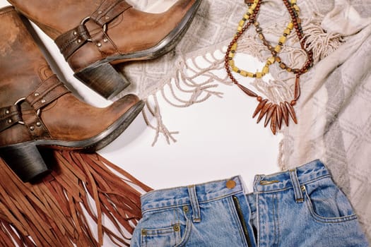 Boho Style. Leather Boots, Wooden Necklace, Denim Shorts and Hippie Bag with Fringe on White Background. Overhead View of Woman's Casual Day Outfits. Trendy Hipster Look.