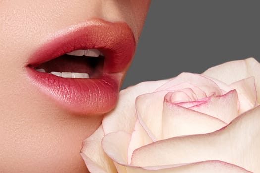 Close-up macro of beautiful female lips with bright kissed makeup. Sexy red lip make-up with gold glitter. Beautiful visage with white rose flower