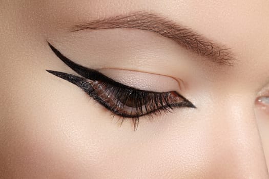 Beautiful macro shot of female eye with classic eyeliner makeup. Perfect shape of eyebrows, brown eyeshadows and long eyelashes. Cosmetics and make-up. Closeup macro shot of fashion liner eyes visage