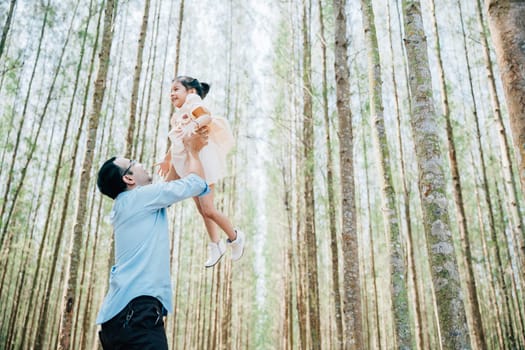Playful family moment, father holds happy little girl up high, throwing up in sky at park forest. cheerful child enjoy moment playing freedom and joy, while loving dad captures precious memory forever