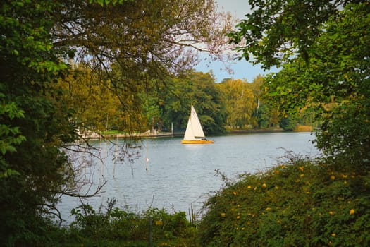 Idyllic lake landscape with sailing boat, framed by green foliage and autumnal trees. Tranquil natural backdrop for relaxation, leisure and enjoyment of nature.