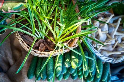 close-up of young greens and vegetables. Green onions in a basket, garlic, cucumbers on the counter of the farmers market. Fresh green vegetables in spring and summer. Concept of vegetarianism, healthy eating. Top view
