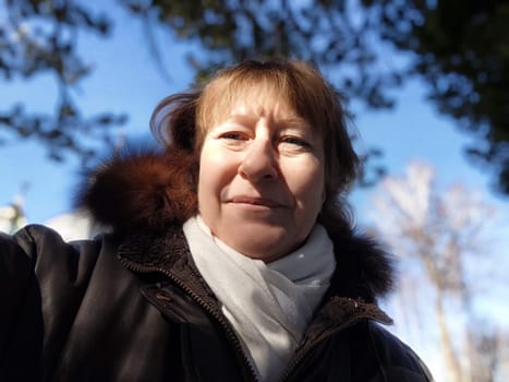 A middle aged woman with blonde hair takes a selfie outdoors, enjoying the beautiful weather while exploring the surroundings.