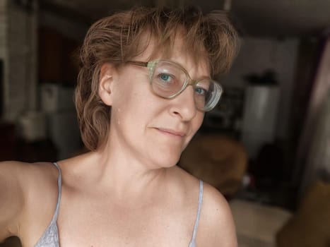Mature woman with glasses enjoys a selfie moment in a relaxed indoor environment, sharing her lifestyle with her followers.