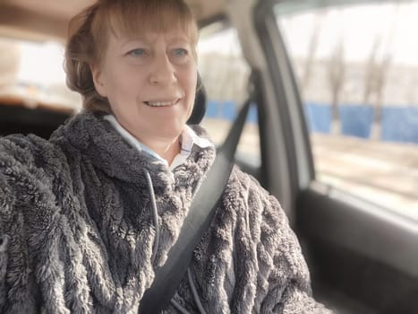 Blonde woman enjoys a cozy moment in her vehicle, capturing a selfie while driving and connecting with her blogging audience on a bright day.