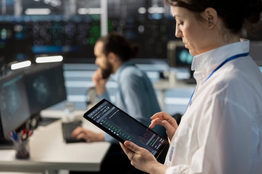Close up of engineer using tablet in data center, managing server virtualization, running scripts. IT specialist using programming language on device in server hub, finetuning network protocols