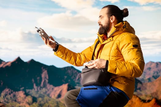 Content creator enjoying the fresh air and filming with his drone, recording professional video on mountain range valley aerial view. Influencer filming his latest travel vlog.