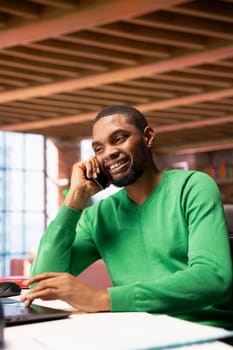 Smiling man at home having friendly conversation with friend over phone call on smartphone. African american person having fun catching up with mate in telephone call, having lively discussion