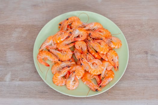 Cooked shrimps arranged neatly on a light green plate, resting on a wooden table, create an inviting and simple seafood presentation that highlights the deliciousness of this meal