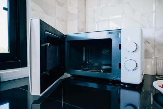 An open microwave oven door on a sleek kitchen tabletop presenting modern technology and design in household appliances. Perfect for showcasing contemporary kitchen equipment.