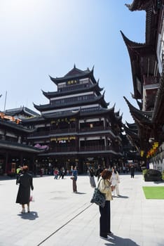 Shanghai, China - 1 April 2025: Tourists walk around the central plaza of Yuyuan Old Street, surrounded by traditional Chinese architecture under clear blue skies