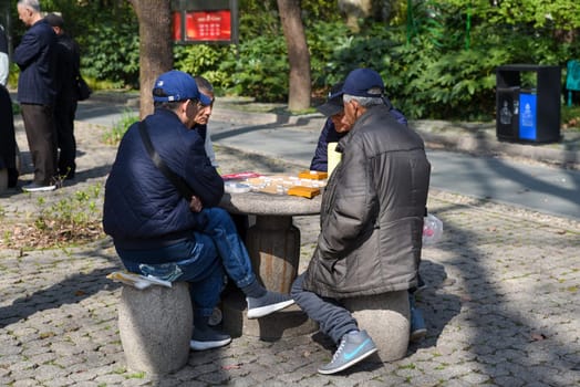 Shanghai, China – 1 April 2025: Elderly Chinese men play Xiangqi (Chinese chess) around a stone table in People's Park on a sunny day, enjoying leisure and tradition