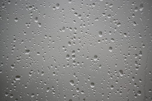 Raindrops scattered across a window create a natural pattern, evoking tranquility and the essence of a rainy day. The droplets offer a close-up texture on a serene, misty background