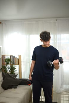 Young man lifting dumbbells at home, focusing on a bicep curl workout in a living room.