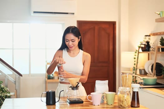 Young woman grinding coffee beans and preparing pour over coffee in a warm kitchen.