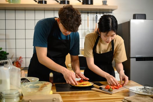 Man and woman decorating pancakes with fruit toppings in a kitchen.