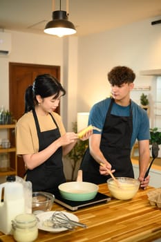 Young couple preparing pancake batter together in a cozy kitchen.