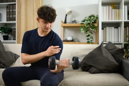 Young man lifting dumbbells on a sofa. Fitness at home concept.