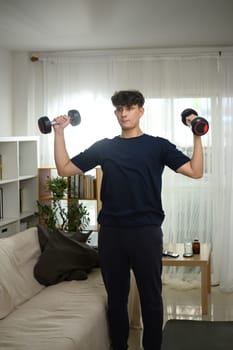 Young man lifting dumbbells at home during a strength training workout.