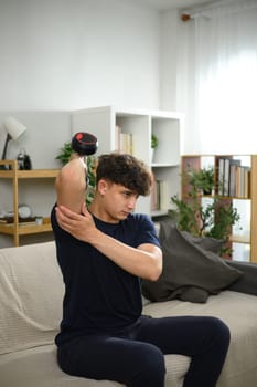 Young man lifting dumbbells on a sofa. Fitness at home concept.