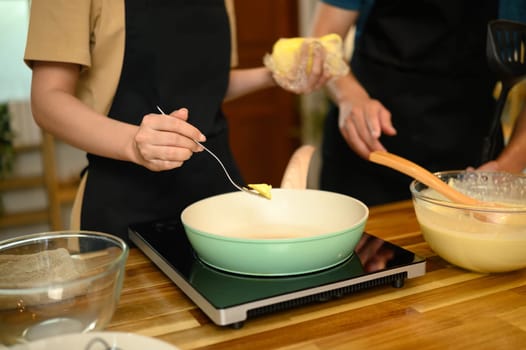 Close up of couple adding butter to pan while preparing pancake batter in kitchen.