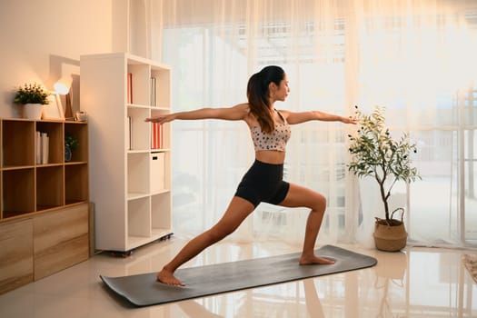 Young woman performing warrior pose on a yoga mat in a living room.