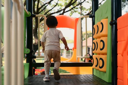 Back view of toddler enjoying playtime at a colorful outdoor playground.