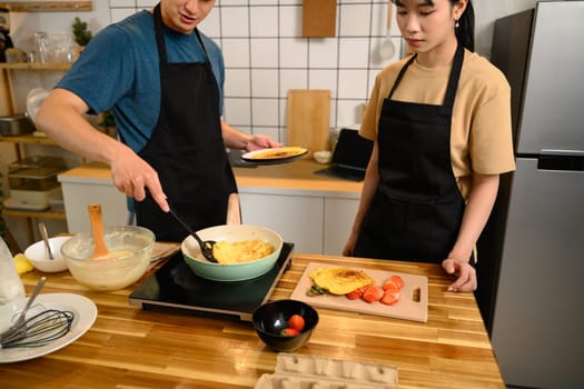 Man and woman making homemade pancakes and slicing fruits for a cozy meal at home.