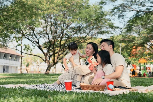 Happy family having a picnic and playing with bubbles together at the park.