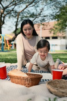 Mother and young child relaxing on picnic blanket in the park, enjoying a sunny day together.