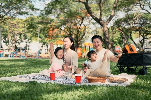 Happy family having a picnic and playing with bubbles together at the park.