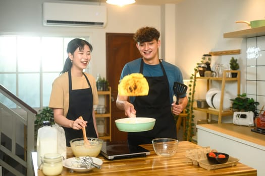 Cheerful couple cooking breakfast in a cozy kitchen, flipping pancakes with smiles and laughter.
