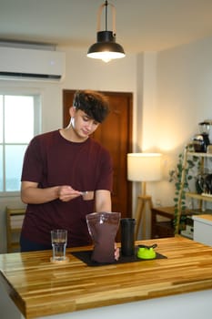Young man preparing a protein shake in the kitchen after workout session.