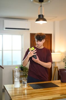 Young man preparing a protein shake in the kitchen after workout session.