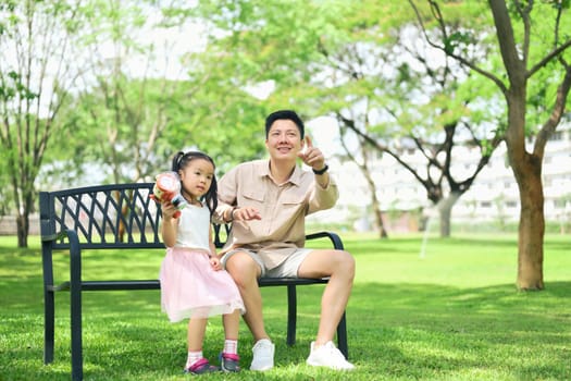 Father and daughter enjoy a sunny day in the park sitting together on a bench.