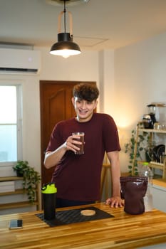 Smiling male holding a glass of chocolate protein drink after exercise.