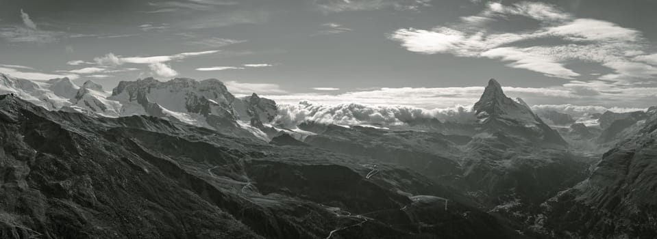 Swiss panoramic landscape photograph of the mountain range near Zermatt, with the iconic Matterhorn towering over beautiful valleys in an alpine scene. Real composite long pano photo in monochrome.