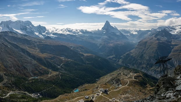Swiss landscape photograph of the mountain range near Zermatt, with the iconic Matterhorn towering over beautiful valleys in an alpine scene. Real composite photo forming a long pano shot.