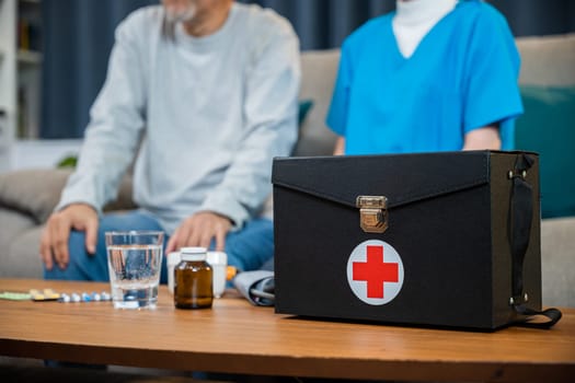 Doctor or nurse in blue medical uniform with fully stocked first aid kit on a wooden table she visit senior man at home or nursing home