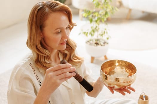 Peaceful woman using a Tibetan singing bowl for mindfulness practice in bright, serene meditation space.