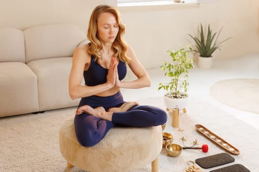Fit woman in lotus pose practicing yoga and meditation indoors with spiritual tools in peaceful home setting.