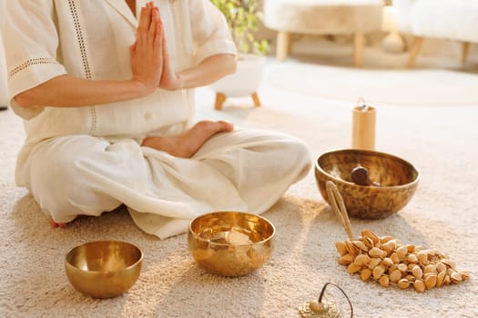 Woman meditating in lotus pose with prayer hands, surrounded by sound bowls and natural wellness tools.