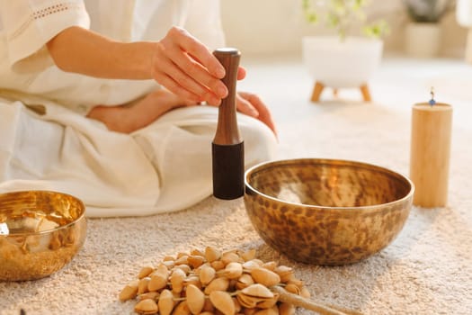 Close-up of woman using Tibetan singing bowl during a sound healing session at home, in peaceful warm light.