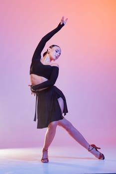 Graceful female dancer in elegant black costume striking a dramatic pose under pink-orange studio lighting.
